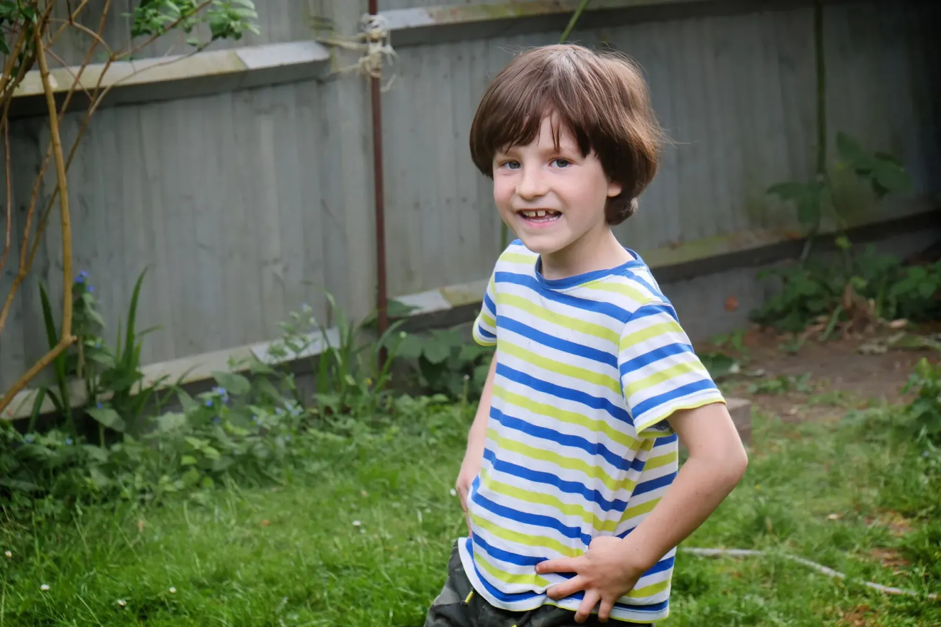A boy stands in front a garden fence.