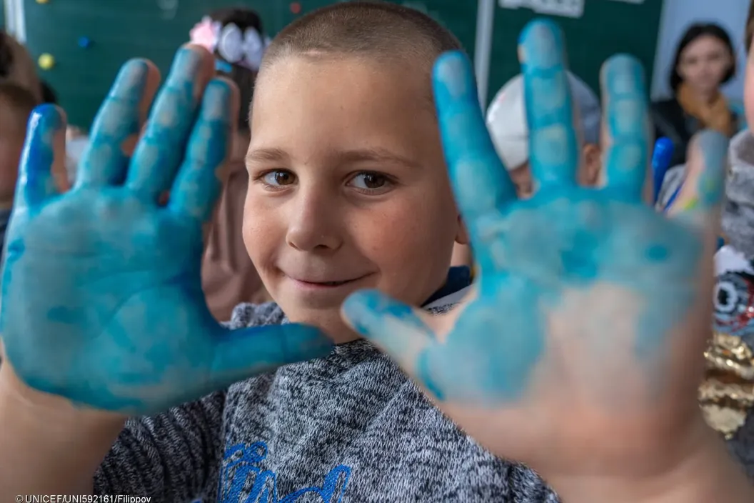 A boy shows his hands painted with blue at the class.